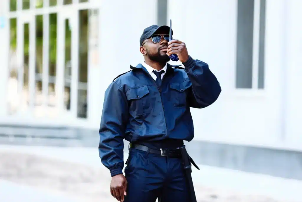 Uniformed security guard speaking into a radio outside a building
